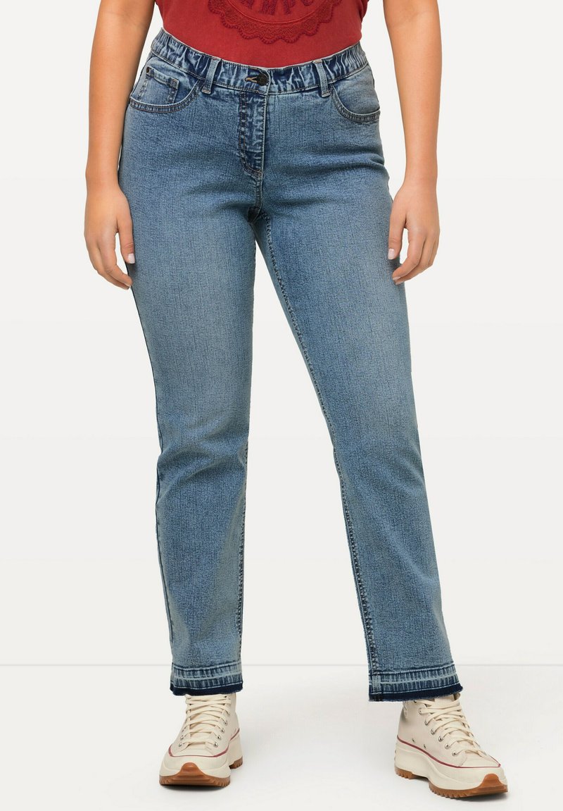 Pantalones vaqueros de un azul claro con una altura media, cinturilla elástica, piernas rectas y costuras en contraste en el dobladillo, combinados con zapatillas beige.