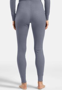 Rear view of a person wearing fitted, high-waisted, long gray leggings and a matching long-sleeve top, standing barefoot on a plain background.