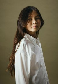 Witte lange mouwen shirt met een kraag, met een iets oversized pasvorm; model heeft donker, golvend haar en een neutrale achtergrond.