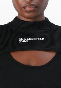 Collo a rotondo nero a coste con dettaglio a taglio, con logo bianco "KARL LAGERFELD JEANS" sul petto. Texture liscia, design aderente.