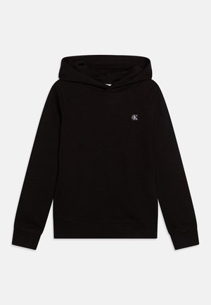 Sweat-shirt à capuche noir à manches longues, avec poignets et ourlet côtelés, et petit logo blanc "cK" sur la poitrine gauche.
