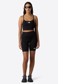 Crop top de sport noir et shorts taille haute, tous deux en matière extensible, avec des accents de logo blanc discrets et un design épuré et minimaliste.