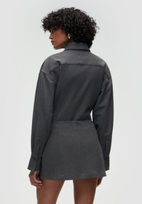 Abito grigio strutturato con maniche lunghe, dettagli con bottoni sui polsini e una silhouette rifinita. Il tessuto sembra liscio con una texture sottile.