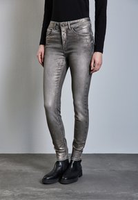 Metalliskt silverfärgade skinny jeans med hög midja, fem fickor och en slät textur, tillsammans med svarta ankelskor.