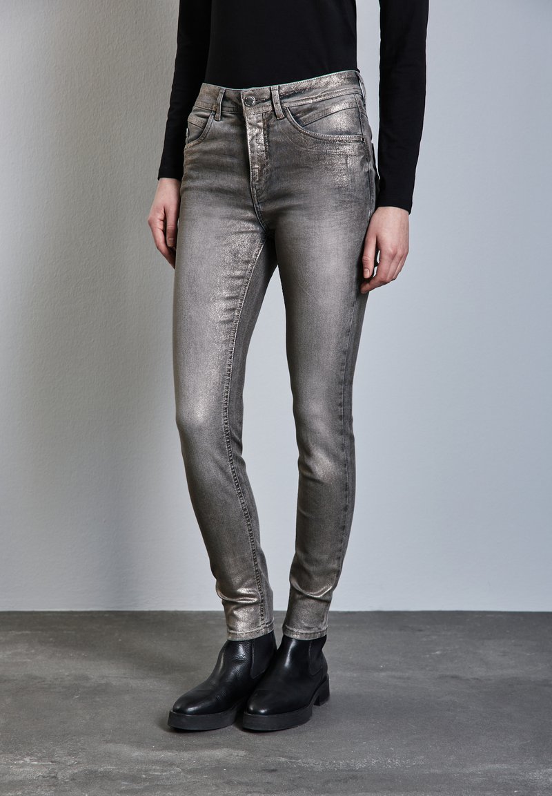 Metalliskt silverfärgade skinny jeans med hög midja, fem fickor och en slät textur, tillsammans med svarta ankelskor.