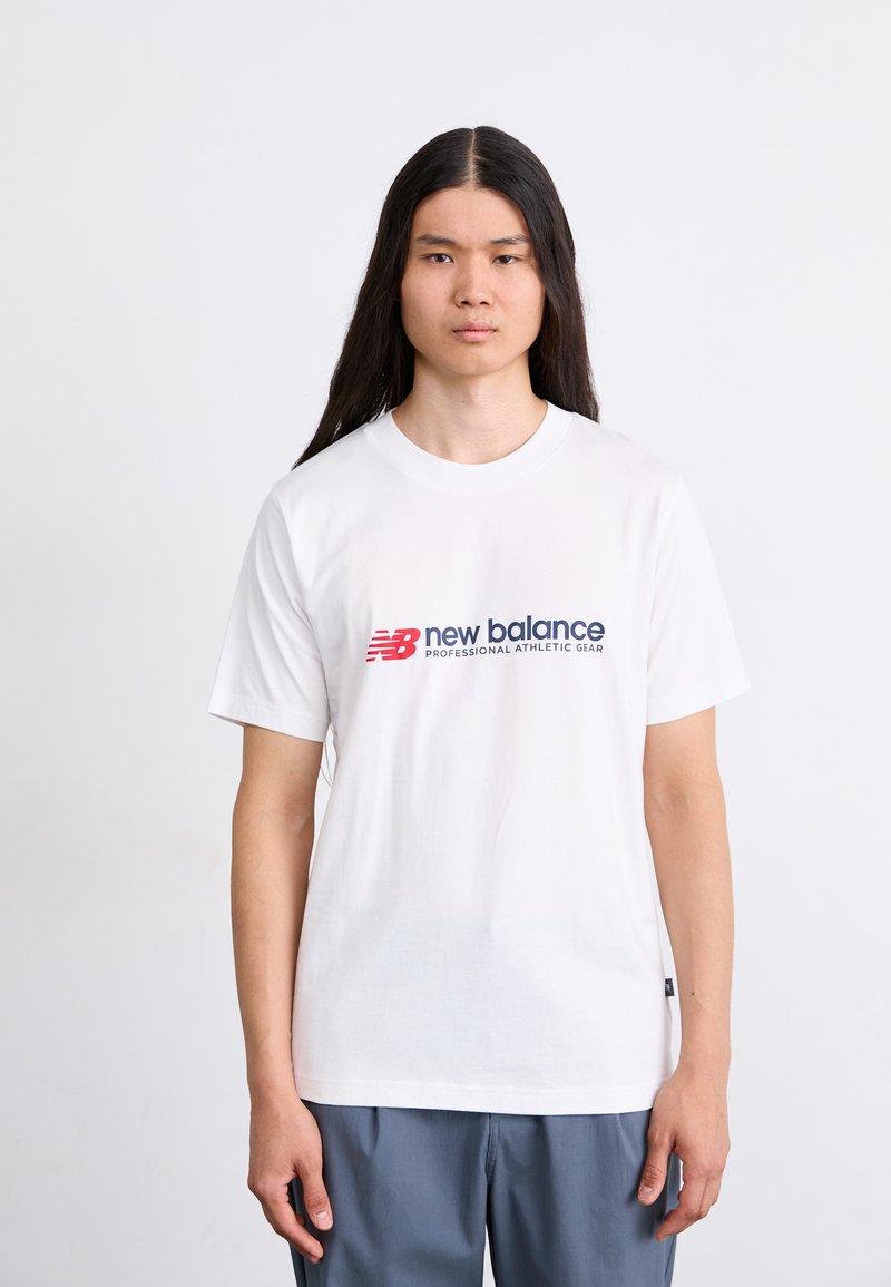 Camiseta blanca de algodón con el logo de "new balance" en rojo y azul. Corte relajado, mangas cortas y cuello redondo. Diseño simple, sin patrones.