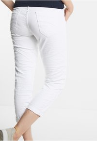 Witte katoenen broek met een taps toelopende pasvorm en opgerolde pijpen, voorzien van twee achterzakken en subtiele gestructureerde details.