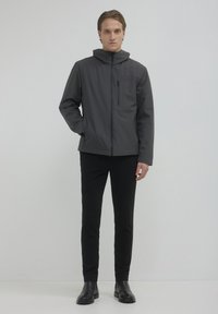 Graue wasserdichte Jacke mit hohem Kragen, Frontreißverschluss und Seitentaschen, kombiniert mit schwarzen Hosen und Stiefeletten. Minimalistisches Design.