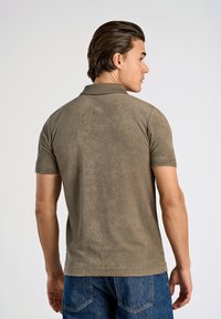 Polo shirt verde oliva scuro con maniche corte, texture morbida e colletto classico. Indossato con jeans in denim blu, visto da dietro.