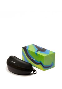 Fekete keménytok napszemüveghez, cipzárral, egy zöld és kék mintás doboz mellett elhelyezve, amelyen a "HAWKERS" felirat található.