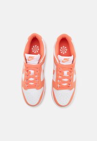 Paire de baskets Nike blanches et corail avec des lacets corail et un logo Nike orange sur la languette, vues de dessus.
