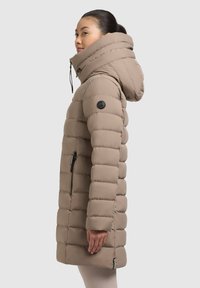 Jachetă puffer bej cu glugă supradimensionată, quilt vertical, buzunare laterale cu fermoar și patch negru cu logo pe mâneca stângă. Textură netedă și elegantă.