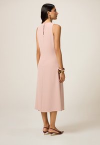 Abito midi senza maniche color rosa pallido con una vestibilità dritta, dettaglio a chiave sulla schiena e texture liscia; abbinato a scarpe burgundy con tacco basso.