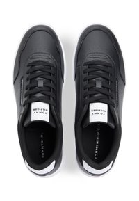 Μαύρα συνθετικά αθλητικά παπούτσια με λείο υφή, άσπρη σόλα και αντιθετικό λογότυπο στη γλώσσα και το πλάι. Διαθέτουν διάτρητη λεπτομέρεια και κορδόνια.