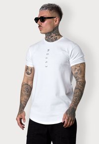 White cotton t-shirt with short sleeves featuring vertical black text "ESTEM." Model wearing black sunglasses, visible tattoos on arms.