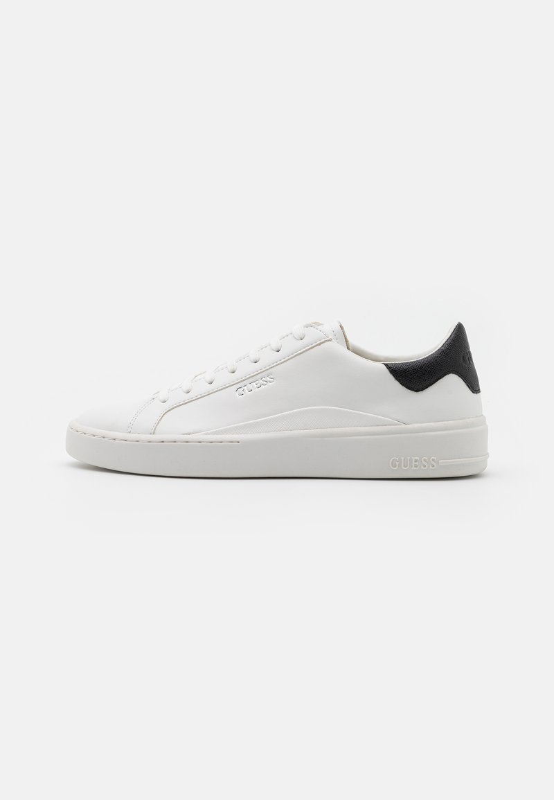 Baskets blanches basses avec lacets blancs, semelle épaisse, détail noir au talon et logo GUESS embossé sur le côté. Placées sur un fond uni.