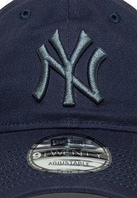 Tumši zils beisbola cepures izgatavots no auduma ar izvirzītu sudraba izšuvumu "NY" logo. Iespējo uzsistāmu siksniņu un apaļo birku ar uzrakstu "9TWENTY."