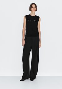 Black sleeveless top with two front pockets and silver hardware, paired with wide-leg black pants. Smooth fabric and tailored fit.