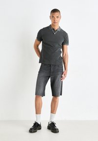 Camisa polo gris oscuro, pantalones cortos de mezclilla negros y zapatos negros con cordones. Los pantalones cortos son hasta la rodilla con bordes deshilachados. Los calcetines blancos son visibles.