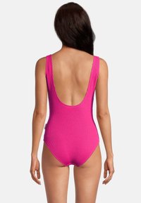 Maillot de bain une pièce fuchsia avec une texture côtelée, un dos décolleté et des bretelles larges. Présente une ouverture de jambe échancrée et un détail d'étiquette sur le côté.
