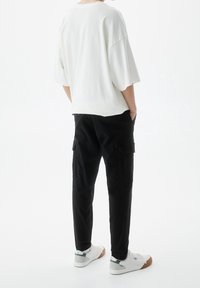 Witte oversized t-shirt met verlaagde schouders, gecombineerd met zwarte cargo-broeken met zijzakken. Schoeisel: witte sneakers met grijze accenten.