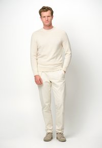 Beige Strickpullover, cremefarbene Hose und helle Sneakers. Der Pullover hat gerippte Bündchen und einen Saum mit einem schlichten, strukturierten Finish.