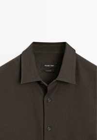 Chemise boutonnée col à revers de couleur brun foncé avec deux boutons visibles, arborant une étiquette "Massimo Dutti" à l'intérieur du col.