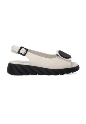 Beige slingback sandal with a peep toe, large black accent, and a textured black sole featuring a twisted pattern. Adjustable buckle closure.