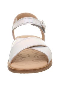 Weiße Sandale mit Kreuzriemendesign, glänzender Oberfläche, verstellbarem Schnallenverschluss und einem strukturierten beigen Fußbett mit kreisförmigen Mustern. Flache Sohle.