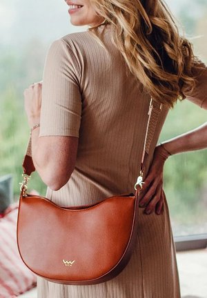 Braune Leder-Schultertasche mit abgerundeter Form, goldenen Hardware-Details und einem abnehmbaren Kettenriemen. Gestreiftes beiges Kleid teilweise sichtbar.