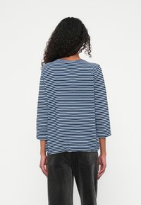 Striped long-sleeve top with a round neckline in navy and light blue, made of soft fabric, paired with dark corduroy pants. Back view displayed.