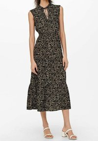 Svart klänning med leopardmönster, korta ärmar och knytning vid halsringningen. Utsådd midi-kjol som bärs med vita sandaler.