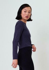 Langarm, cropped top in marineblau stof. Kenmerkt zich door een ronde halslijn en aansluitend ontwerp, gecombineerd met zwarte high-waisted leggings.