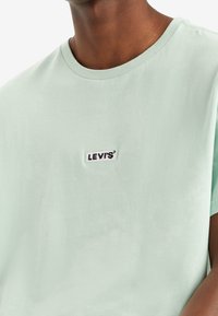 Light green cotton T-shirt with a round neckline and short sleeves. Features a small black and white "LEVI'S" logo patch on the front.