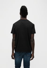 Μαύρο βαμβακερό t-shirt με στρογγυλή λαιμόκοψη, κοντά μανίκια και απλό πίσω μέρος, σε συνδυασμό με μπλε τζιν παντελόνι.