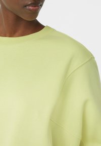 Jasnożółta bluza z ribbowym dekoltem i opadającymi ramionami, wykonana z miękkiego, teksturowanego materiału o luźnym kroju.