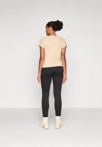 Beige kortärmad topp i kombination med svarta leggings. Toppen har en rundad halsringning och en avslappnad passform; leggings är åtsittande med en slät yta.