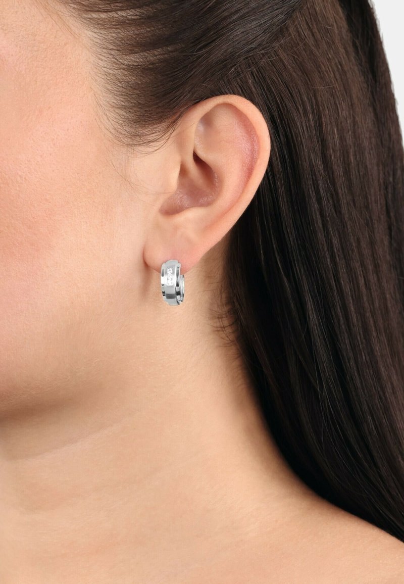 Silver hoopörhängen med en polerad yta, med en slät textur och en kompakt design, bärs i ett piercat öra.