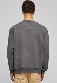 Šedá mikina s texturovaným povrchem, kulatým výstřihem a žebrovanými manžetami. Klasický design se vyznačuje uvolněným střihem a bez viditelného loga.