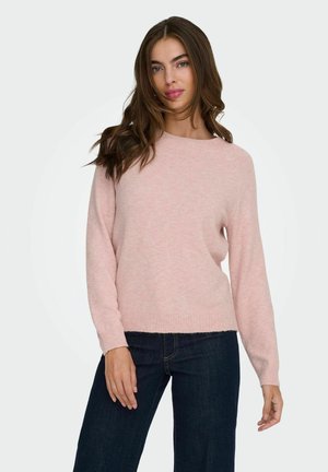 Pull en tricot rose clair avec un col rond, des manches longues et un ourlet droit. Porté avec un jean large noir, offrant une texture douce.
