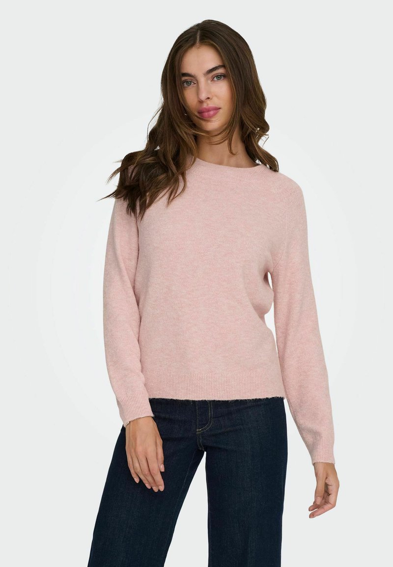 Maglione a maglia rosa chiaro con scollo rotondo, maniche lunghe e orlo dritto. Indossato con jeans larghi neri, caratterizzati da una texture morbida.