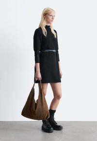 Schwarzes, strukturiertes Kleid mit tailliertem Oberteil und kurzen Ärmeln, kombiniert mit einer braunen Wildleder-Hobo-Tasche und schwarzen klobigen Schnürstiefeln.