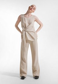 Beige linnen top met zijsstrik, gecombineerd met beige linnen broek met wijde pijpen. Soepele textuur en eenvoudig ontwerp, zonder zichtbare patronen of accenten.