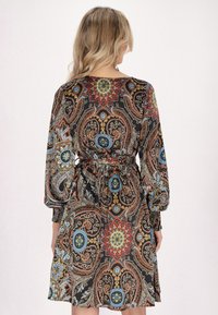 Pitkähihainen musta mekko, jossa on värikäs paisley-kuvio, vyötäröltä kireä ja laskostettu helma.