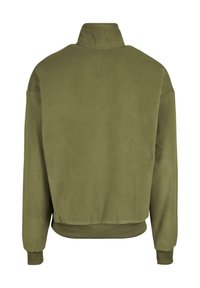 Giacca in fleece verde oliva con collo alto, polsini e orlo a costa. Presenta una texture morbida e una vestibilità rilassata, senza loghi o decorazioni visibili.