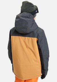 Skijacke in Marineblau, Orange und Schwarz. Verfügt über eine Kapuze und ein strukturiertes Gewebe. Enthält Handschuhe und orangefarbene Schneehose.