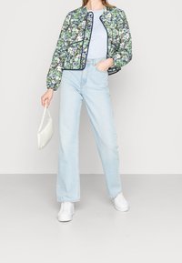 Bloemen gewatteerd jack in groen, blauw en wit, met een ronde halslijn en marineblauwe bies. Gecombineerd met lichtblauwe denim jeans met wijde pijpen en witte sneakers.