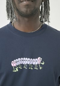 Navy blue short-sleeve T-shirt featuring a colorful cartoon caterpillar graphic with the text "CLEPTOMANICX" in a playful font.