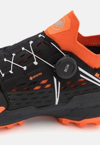 Buty trailowe GORE-TEX w czarnym i pomarańczowym kolorze z usztywnioną cholewką, zintegrowanym systemem sznurowania oraz teksturowaną gumową podeszwą zapewniającą przyczepność.