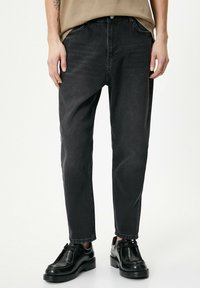 Pantalones de mezclilla negros con un corte relajado, que cuentan con un cierre de botón, cinco bolsillos y un ligero desgaste para dar textura. Combinados con calzado negro.
